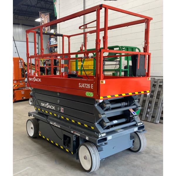 Skyjack SJ4726 E electric scissor lift with red safety railings parked inside an industrial warehouse.