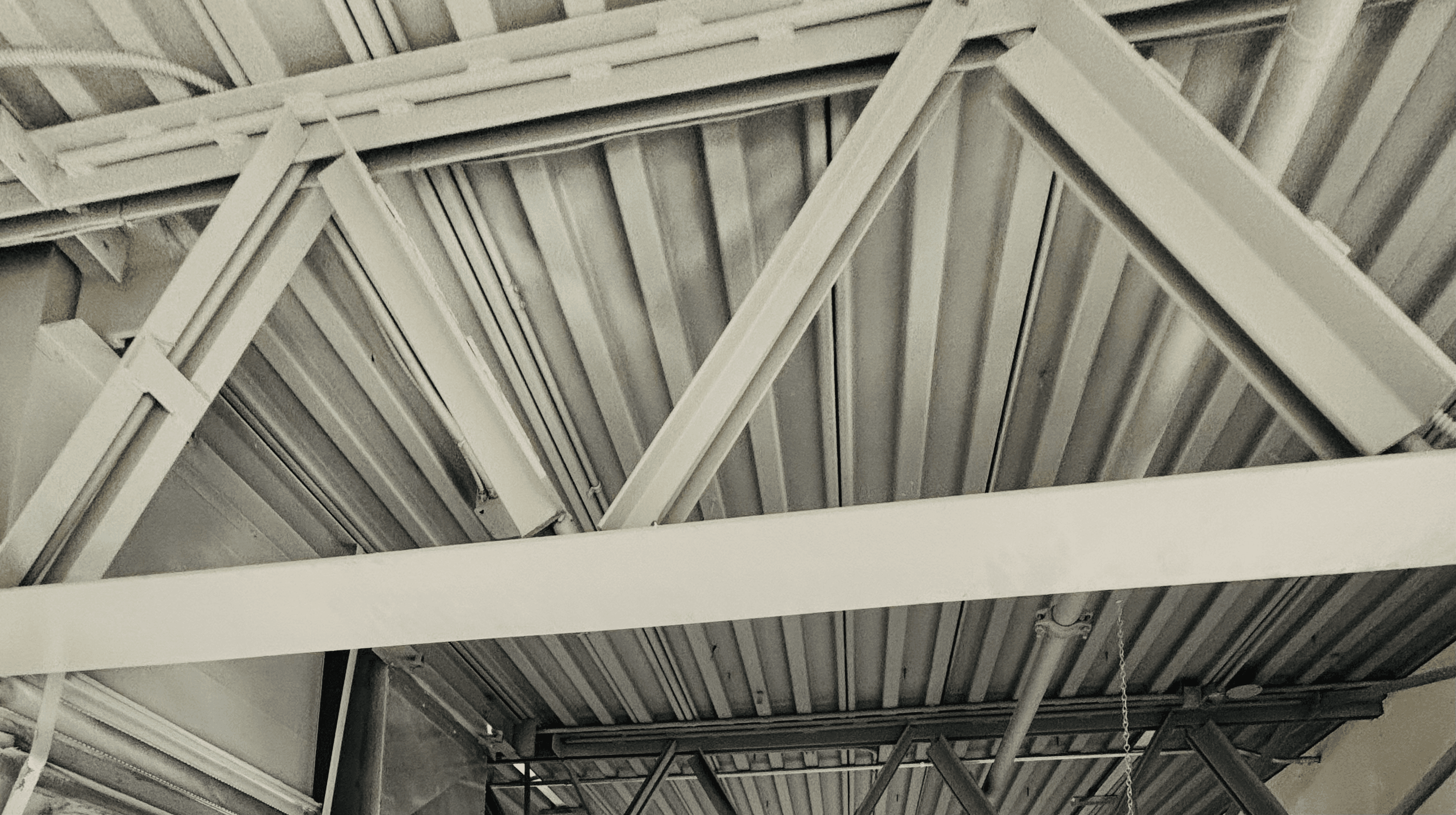 Industrial white-painted ceiling with exposed steel trusses, beams, and corrugated metal roof decking.