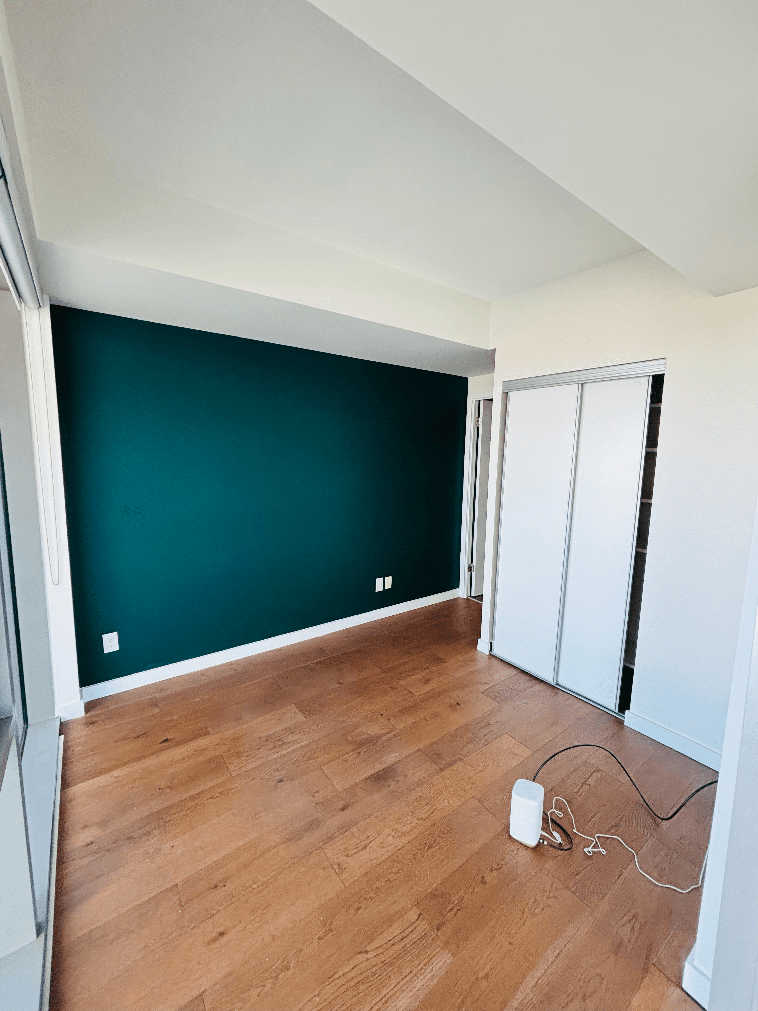 Empty room featuring a dark teal accent wall, hardwood floors, and white sliding closet doors.