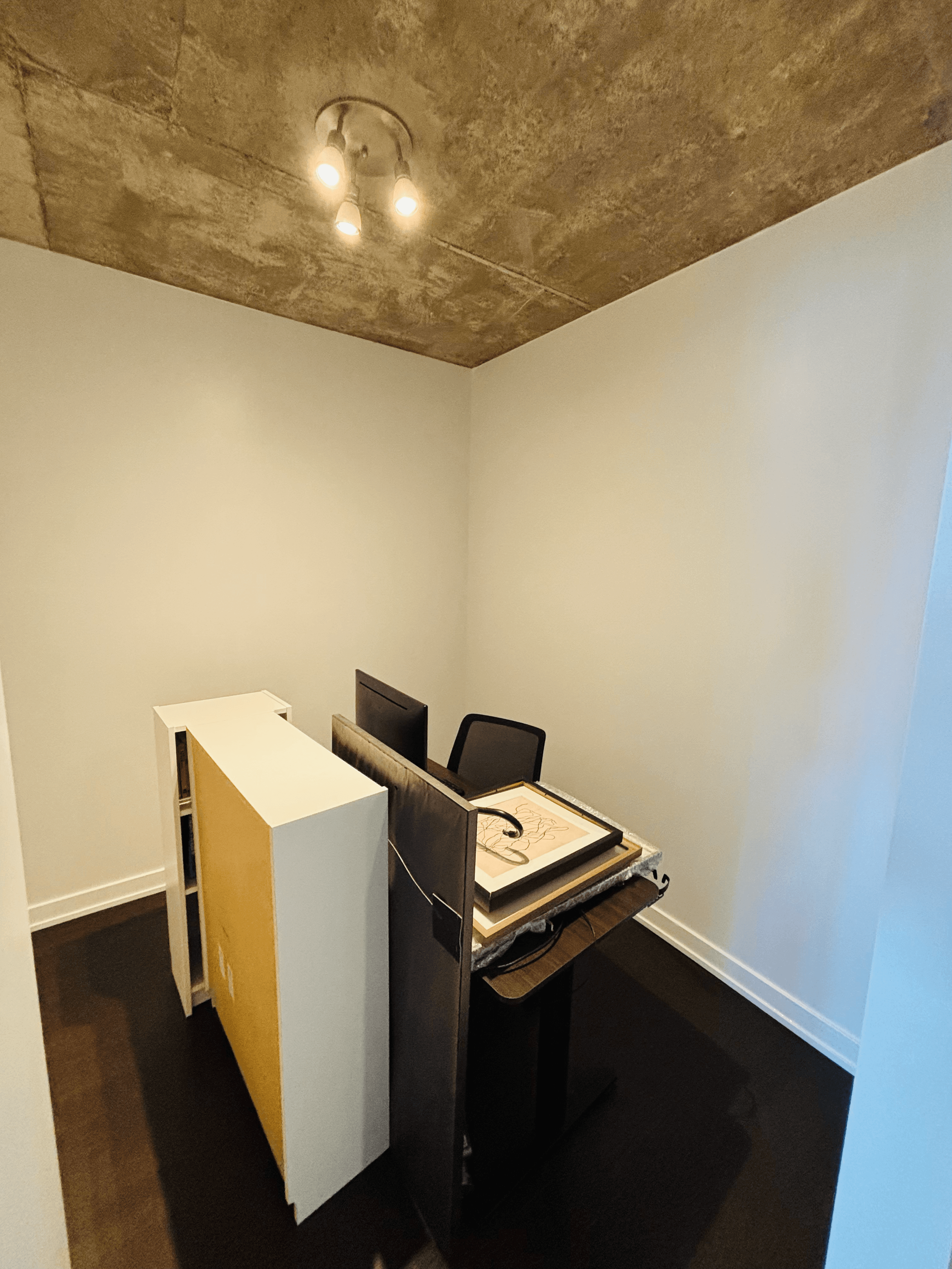 Small office nook with a desk, monitor, and white shelving unit under a concrete ceiling.