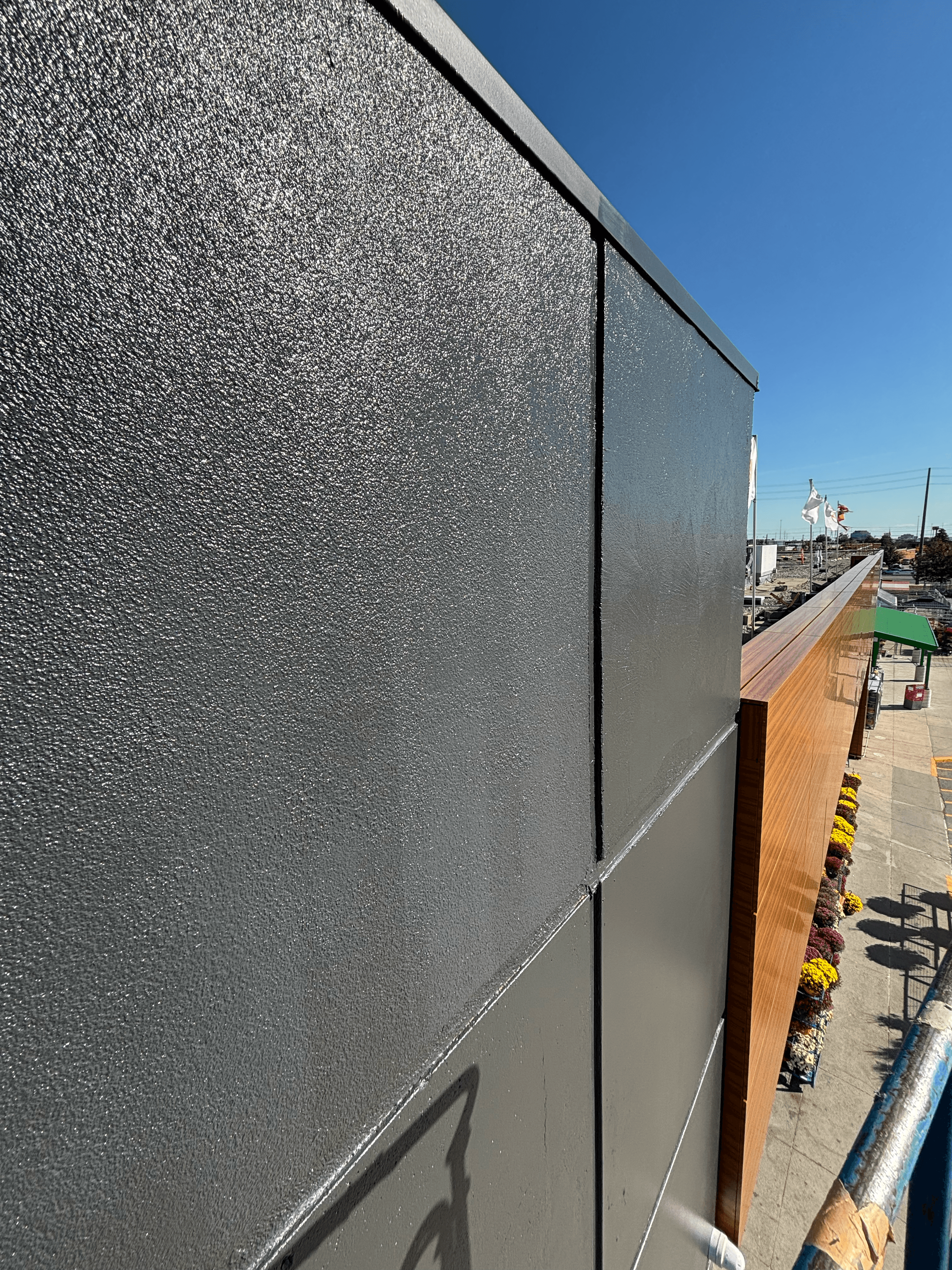 Textured dark grey panels next to a wood-paneled facade with colorful flowers below.