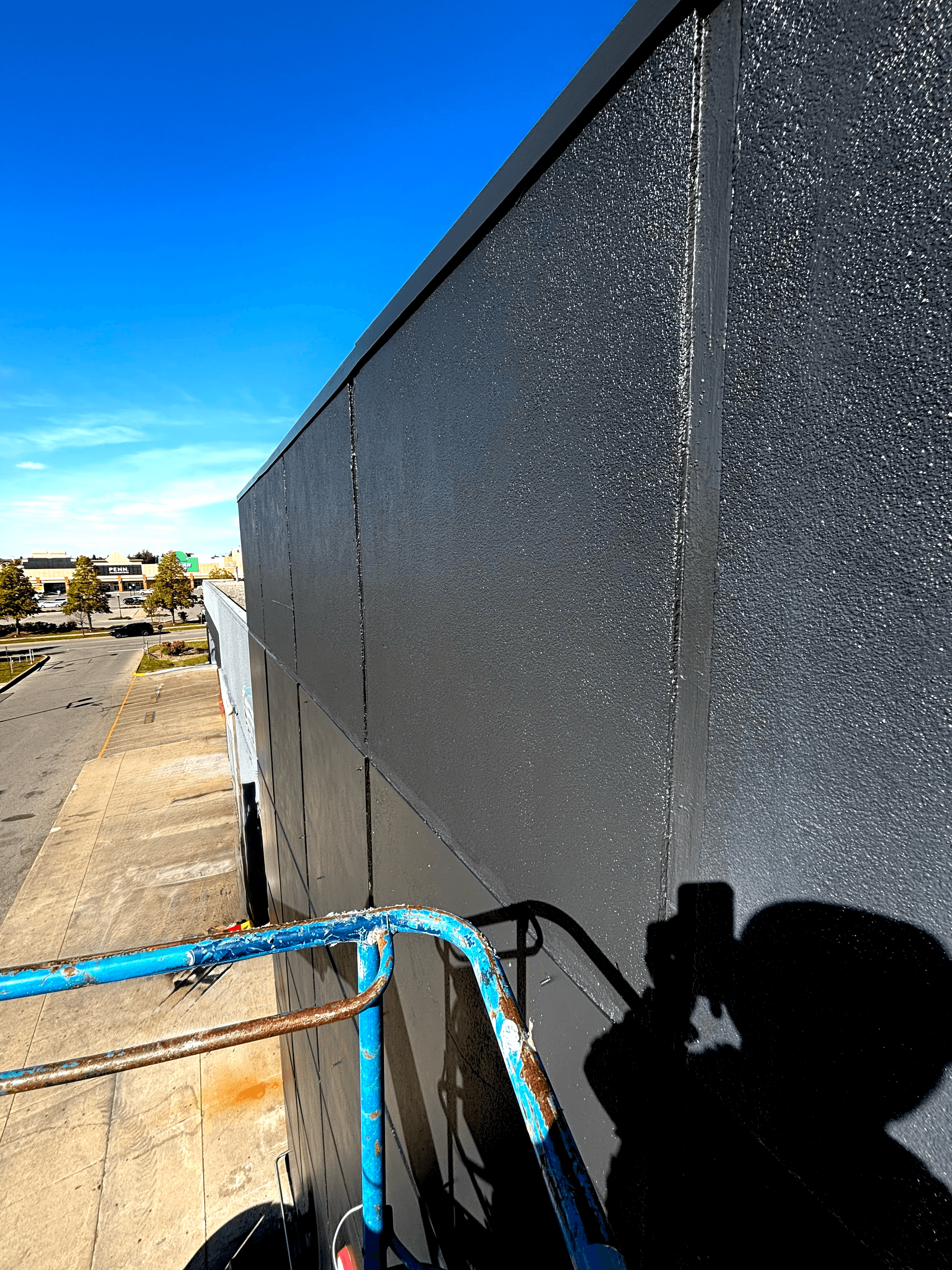 Dark gray textured building wall viewed from a blue lift under a clear blue sky.