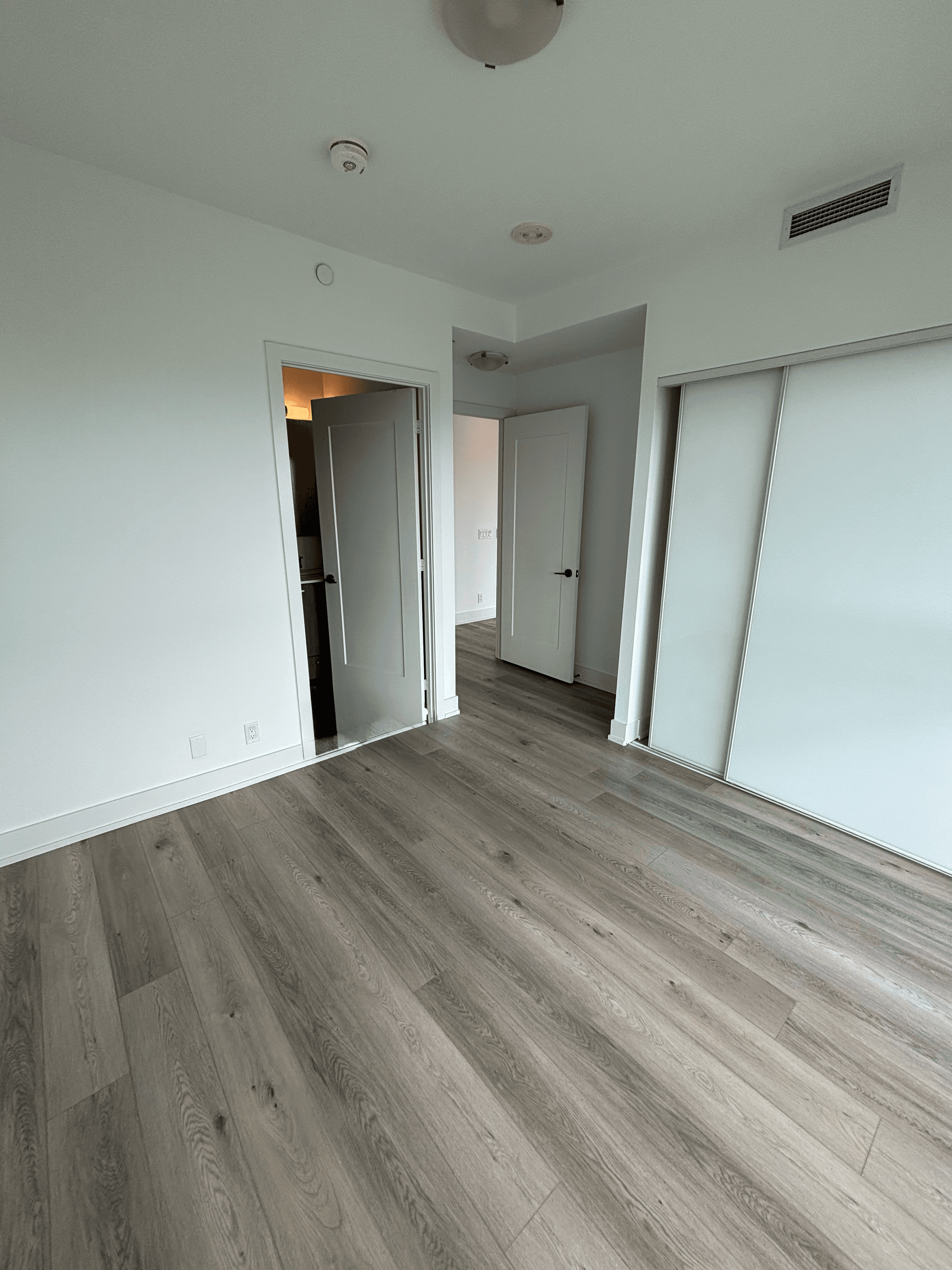 Empty room with light wood flooring, white walls, two open doors, and a sliding closet.