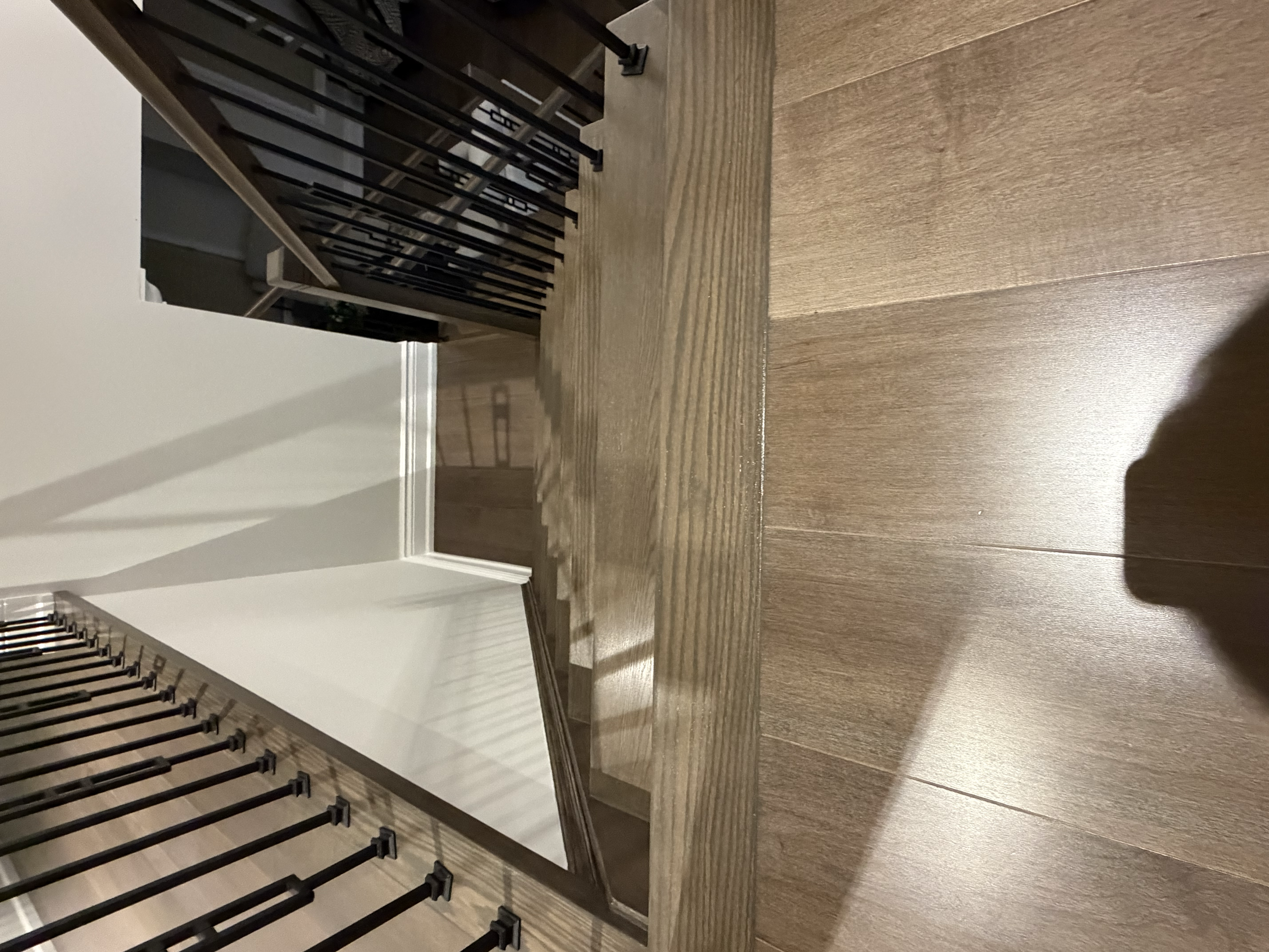 Modern wooden staircase with black metal balusters and white walls, viewed from the top landing.
