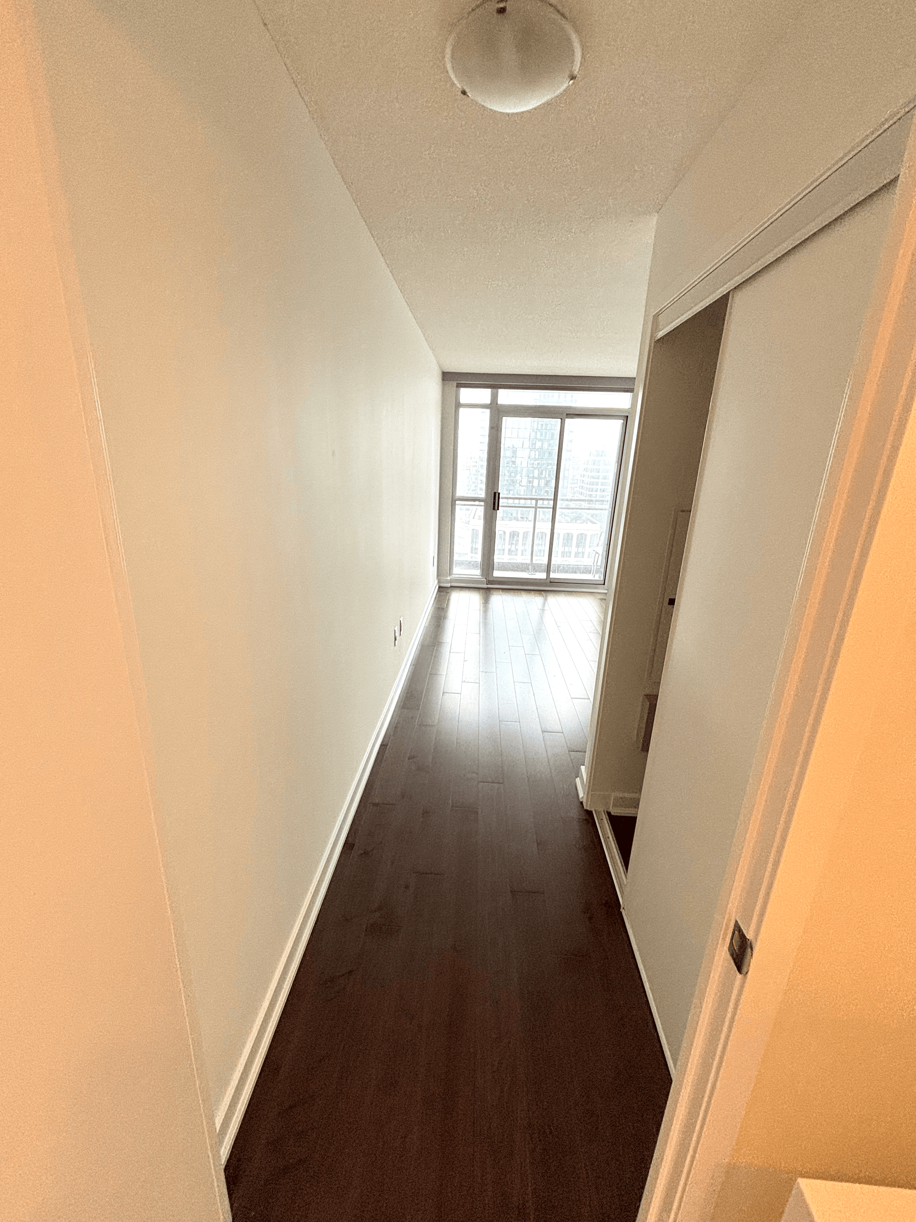 Narrow hallway with dark hardwood floors leading to a sliding glass door with city views.