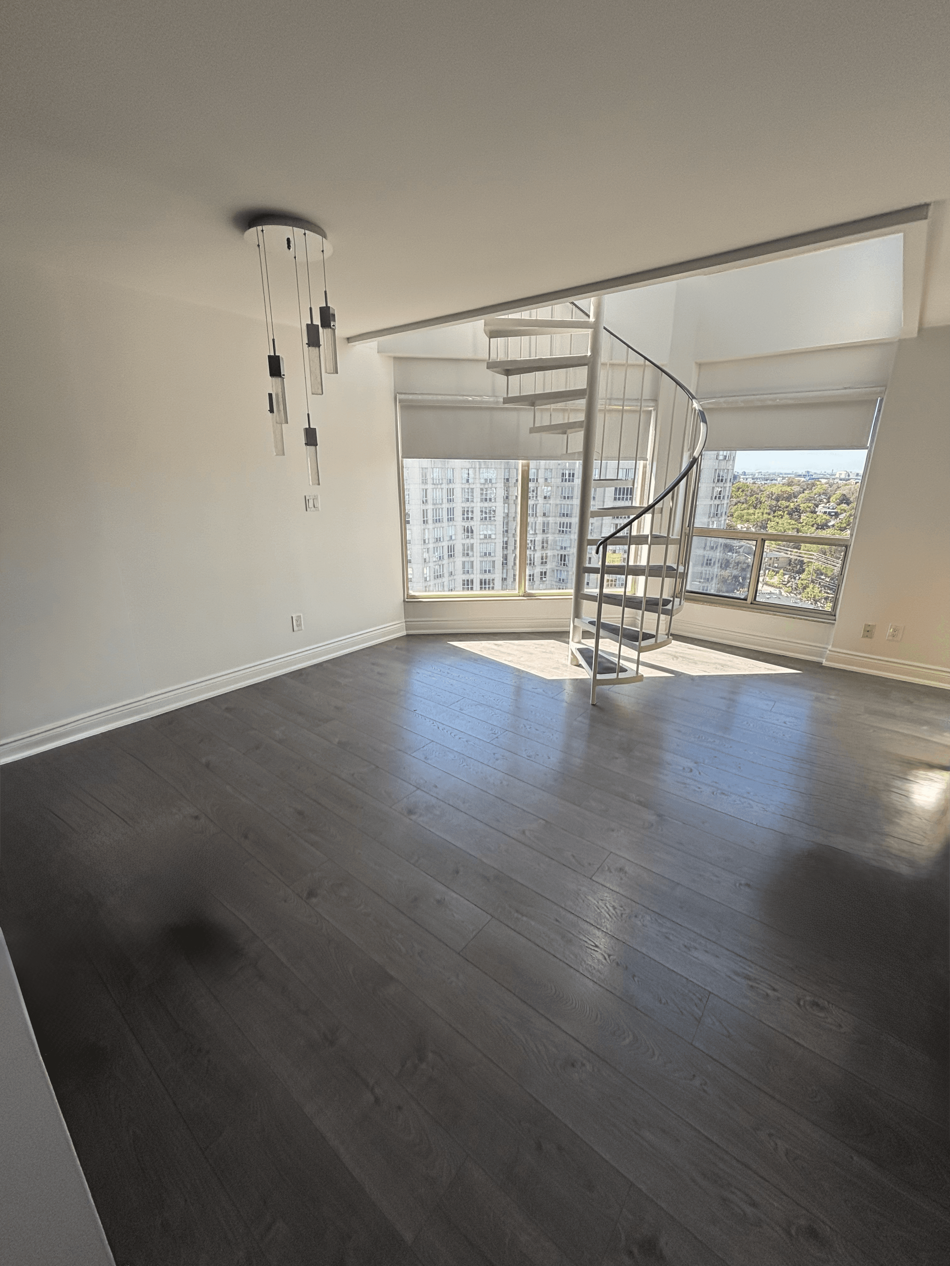Modern empty room with dark wood floors, a white spiral staircase, and large city windows.