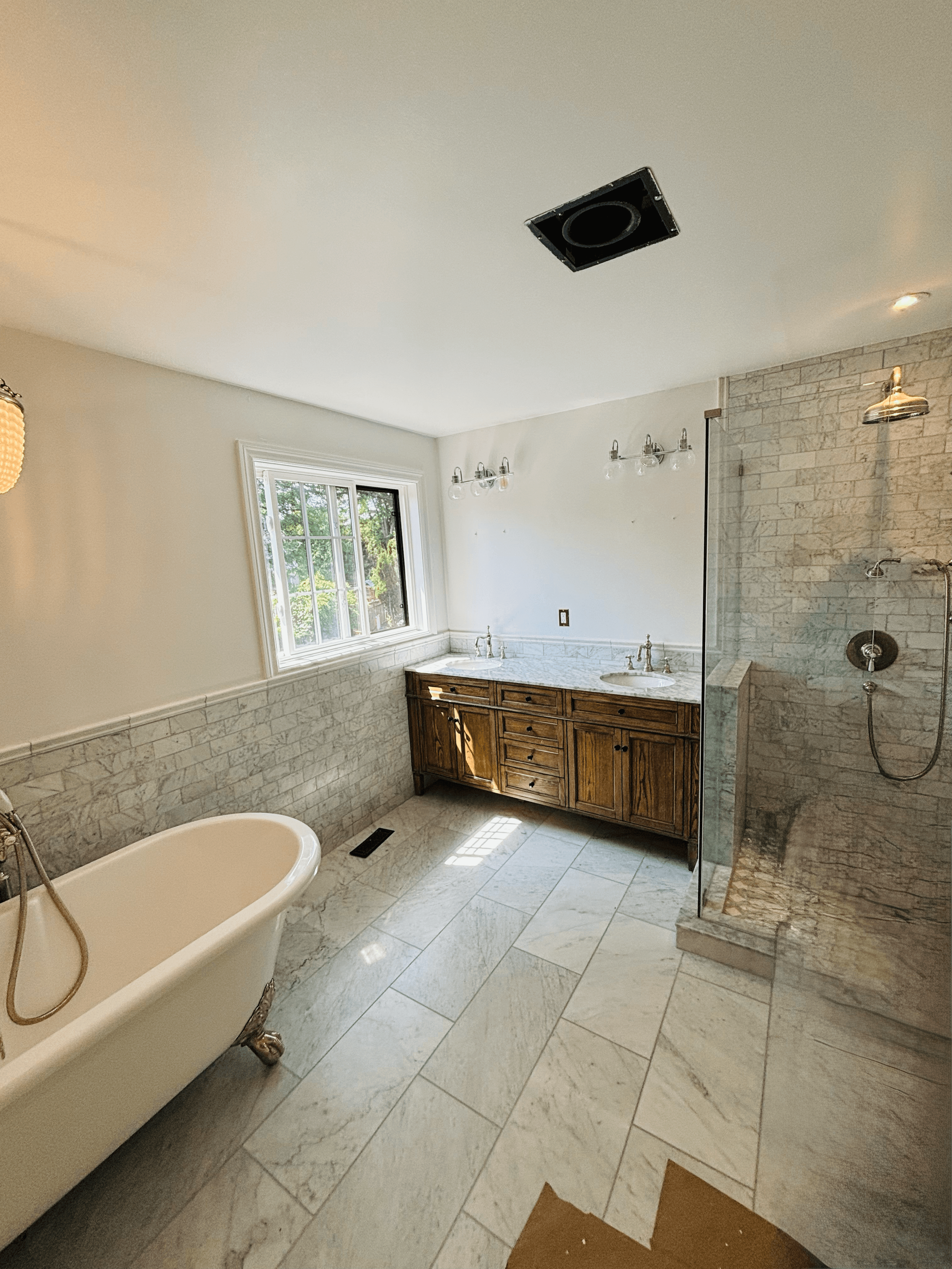 Elegant bathroom featuring a clawfoot tub, wooden double vanity, and a glass-enclosed marble shower.