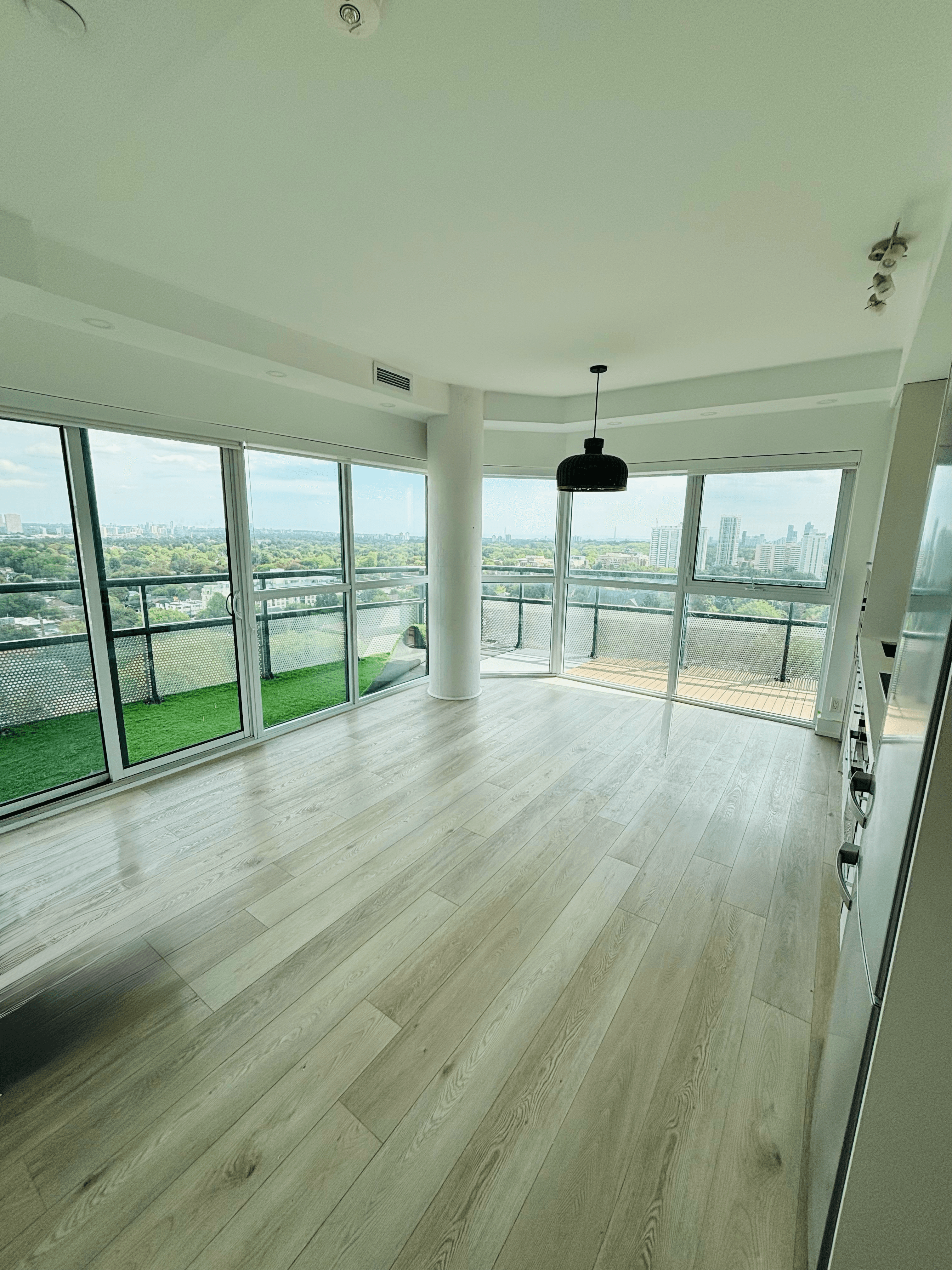 Empty modern apartment with light wood floors and large windows overlooking a city skyline.